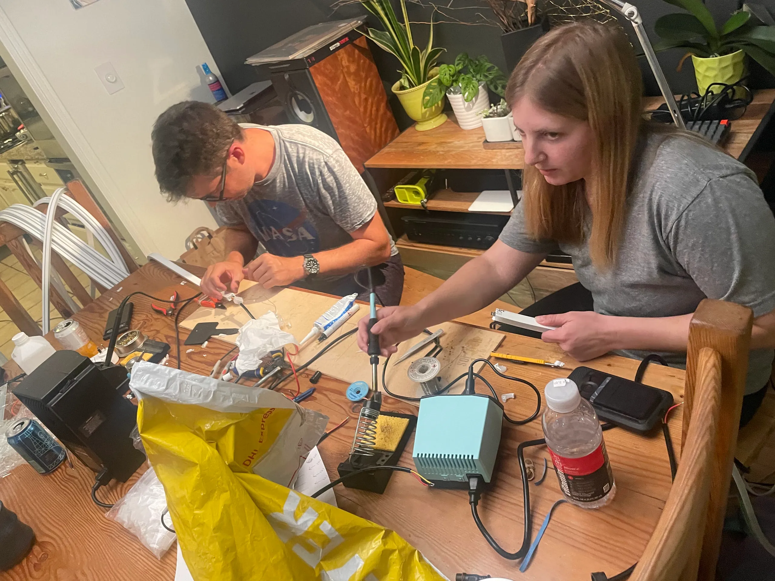 Two crew members soldering LED flame wiring at a kitchen table